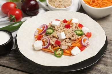 Photo of Delicious tortilla with tuna, vegetables and cheese on wooden table. Cooking shawarma