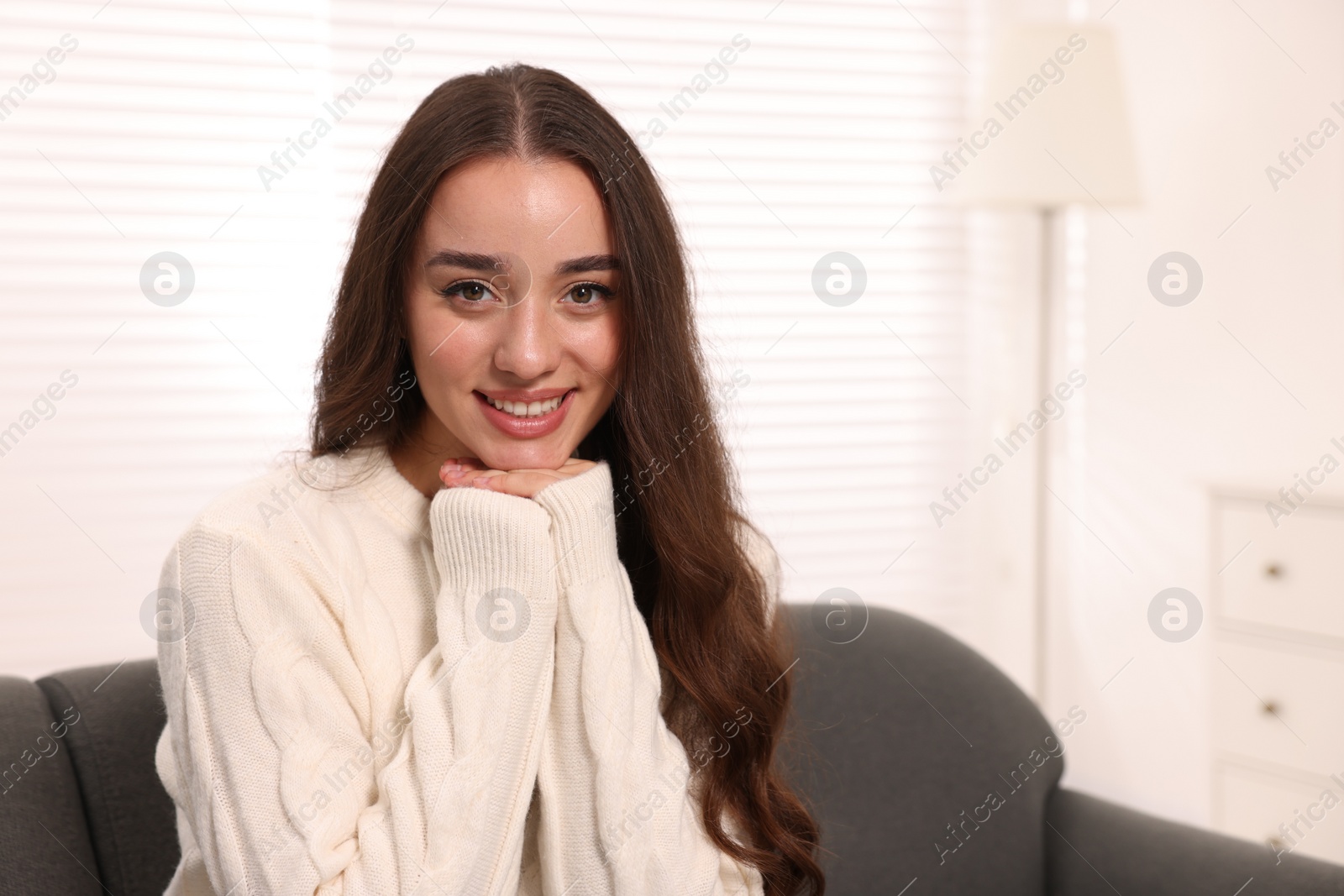 Photo of Beautiful young woman in stylish warm sweater on sofa at home, space for text