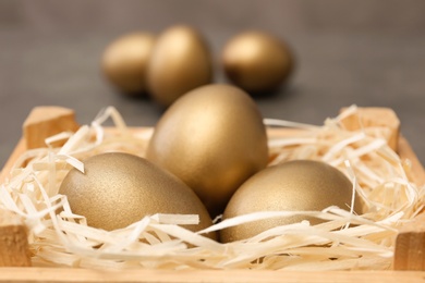 Wooden crate with golden eggs on blurred background, closeup