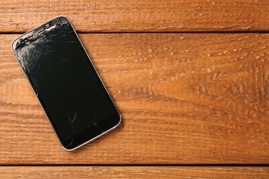 Photo of Damaged smartphone on wooden table, top view with space for text. Device repairing