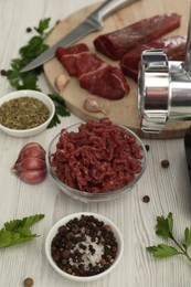 Photo of Meat grinder, beef, garlic, parsley and spices on white wooden table