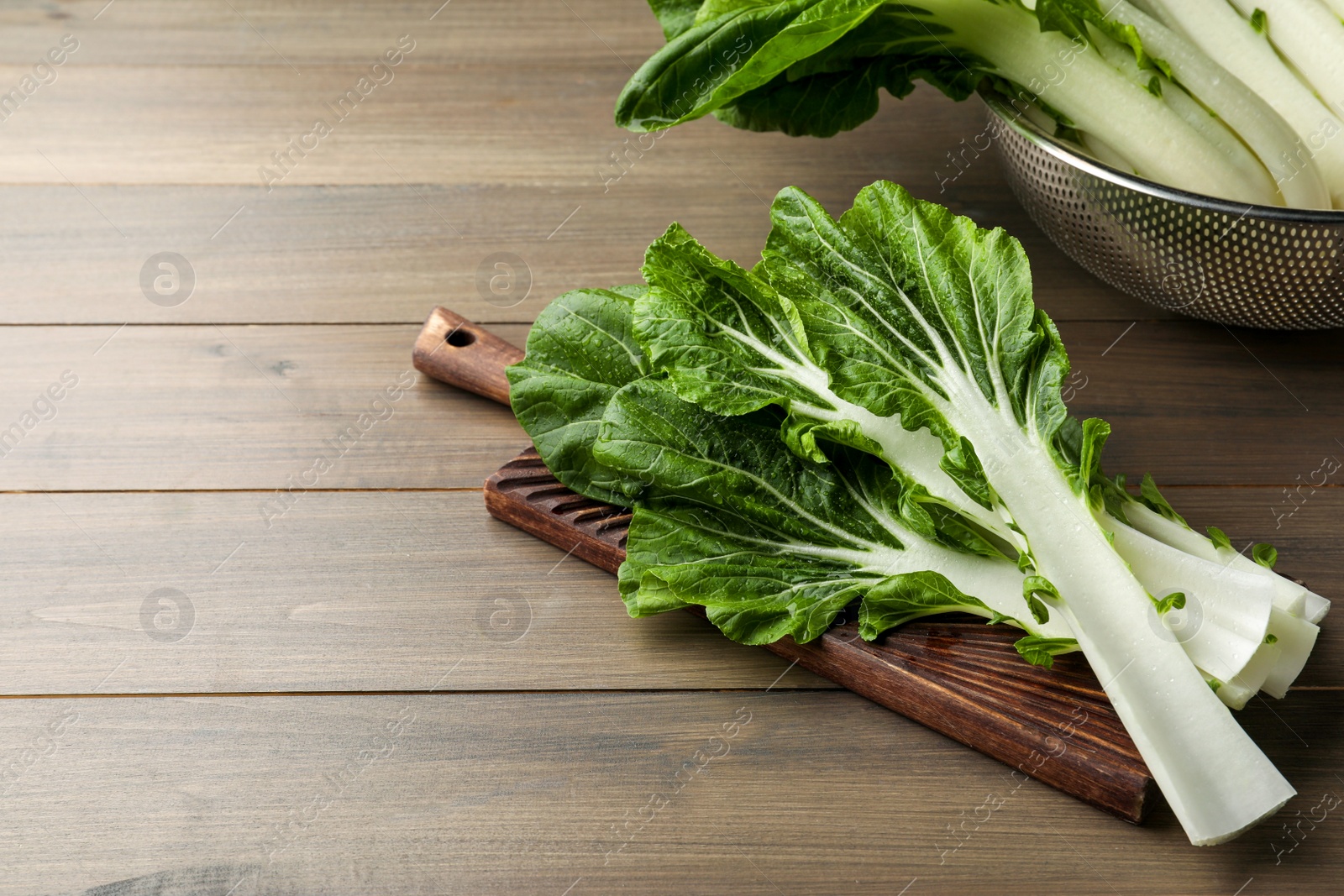 Photo of Leaves of fresh green pak choy cabbage with water drops on wooden table, space for text