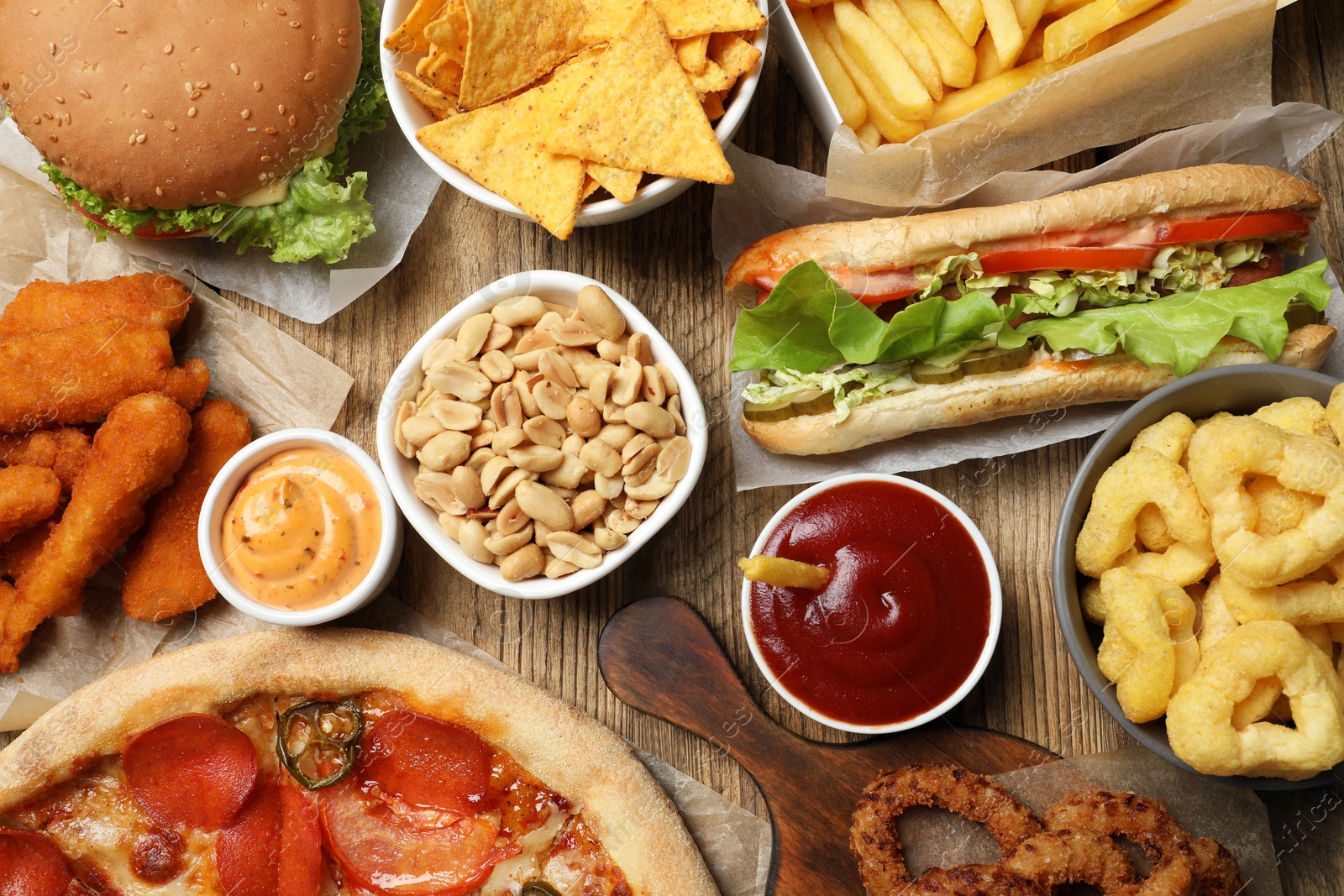 Photo of Onion rings, sandwich and other fast food on wooden table, flat lay