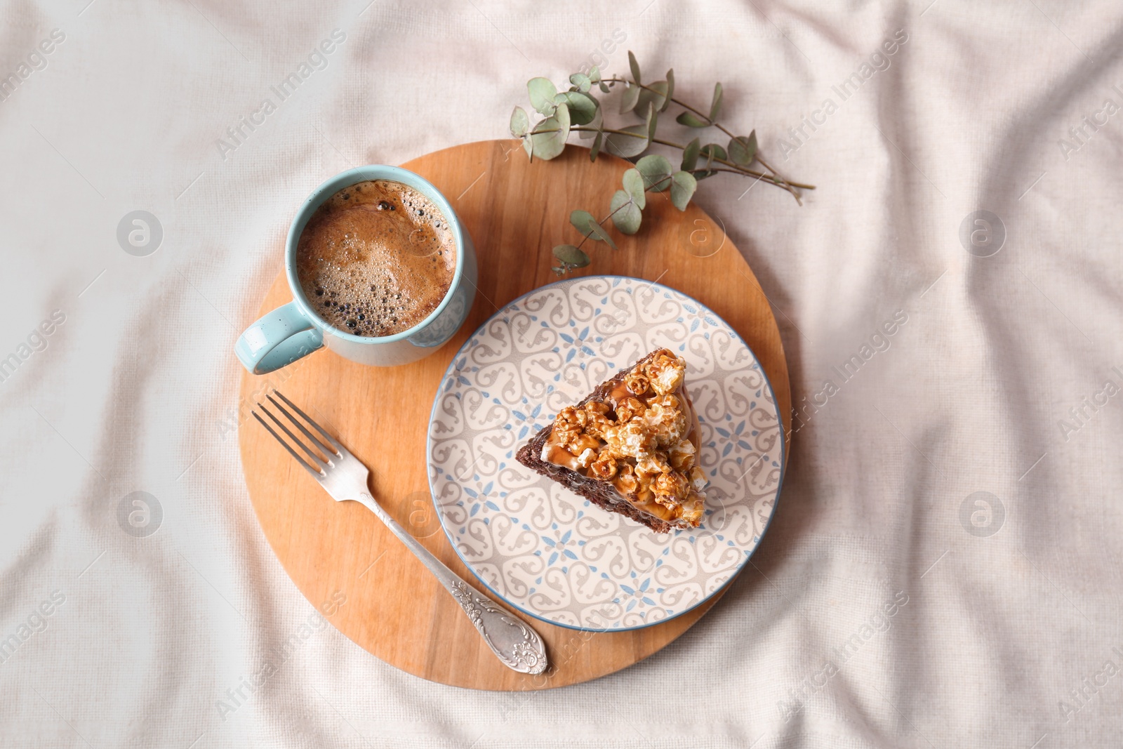 Photo of Piece of delicious homemade cake with caramel sauce and cup of coffee on wooden board, top view