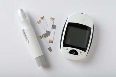 Digital glucometer, lancet pen and test strips on white background, flat lay. Diabetes control