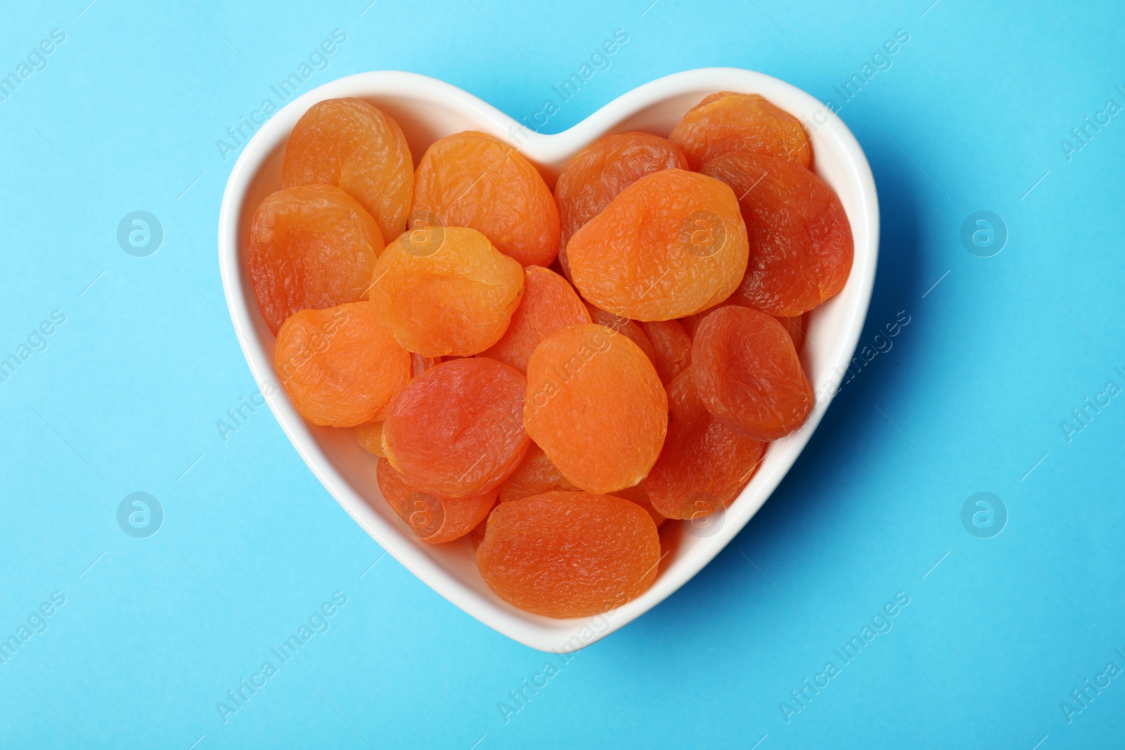 Photo of Bowl with dried apricots on color background, top view. Healthy fruit