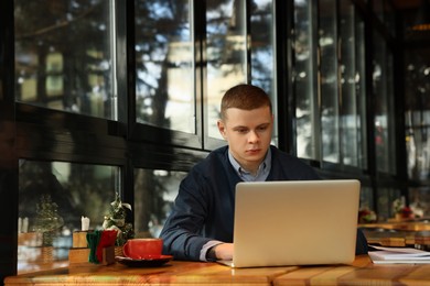 Photo of Young male student with laptop studying at table in cafe