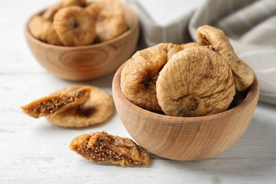 Photo of Wooden bowl of tasty dried figs on white table, closeup