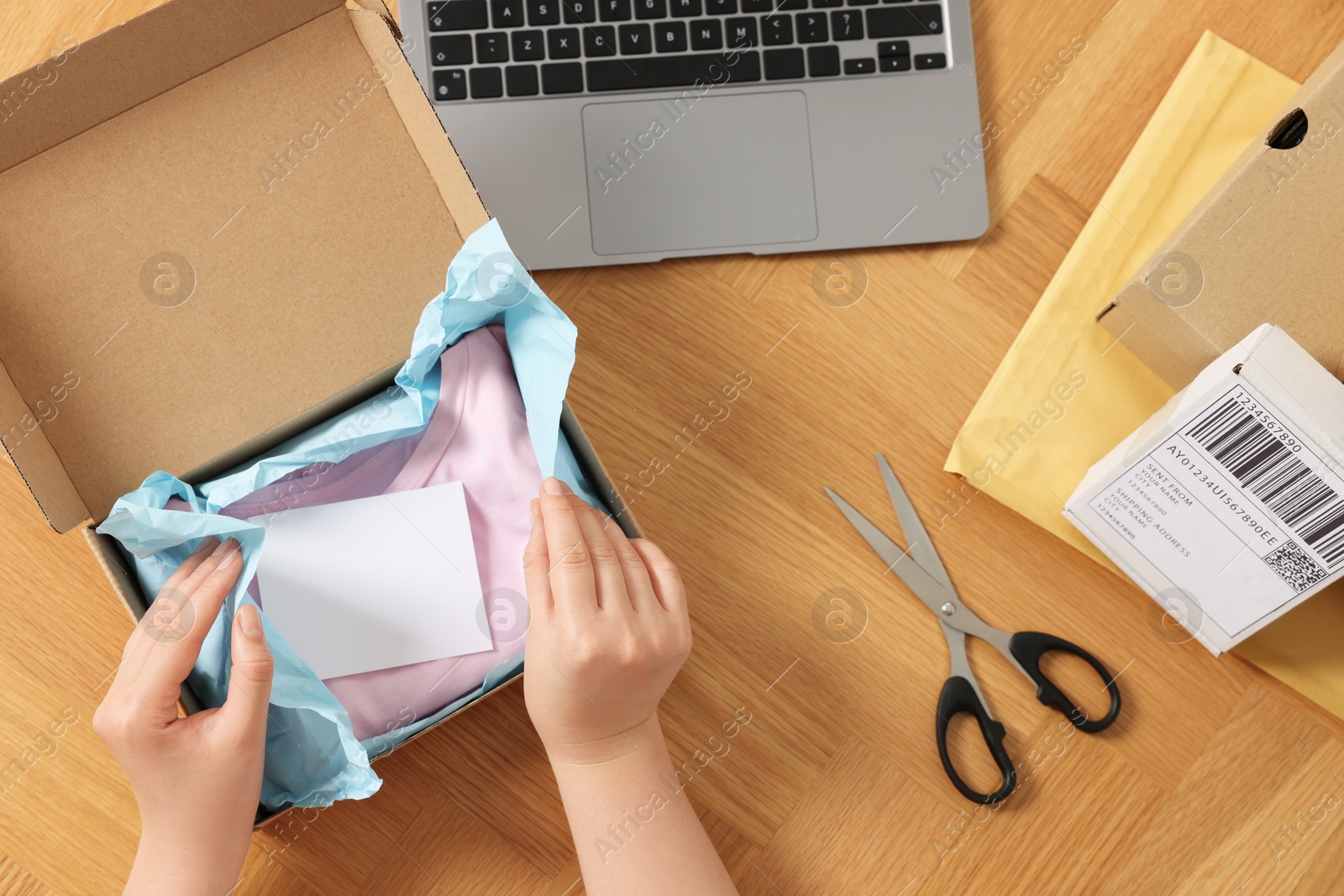 Photo of Woman packing clothes at wooden table, top view. Online store