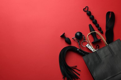 Shopping bag and different sex toys on red background, flat lay. Space for text