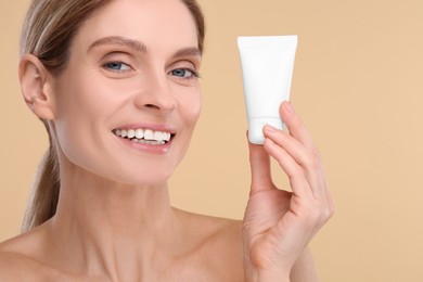 Woman holding tube of foundation on beige background