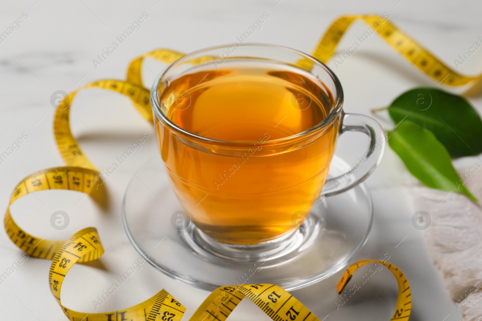 Photo of Cup of herbal diet tea and measuring tape on light table, closeup. Weight loss concept