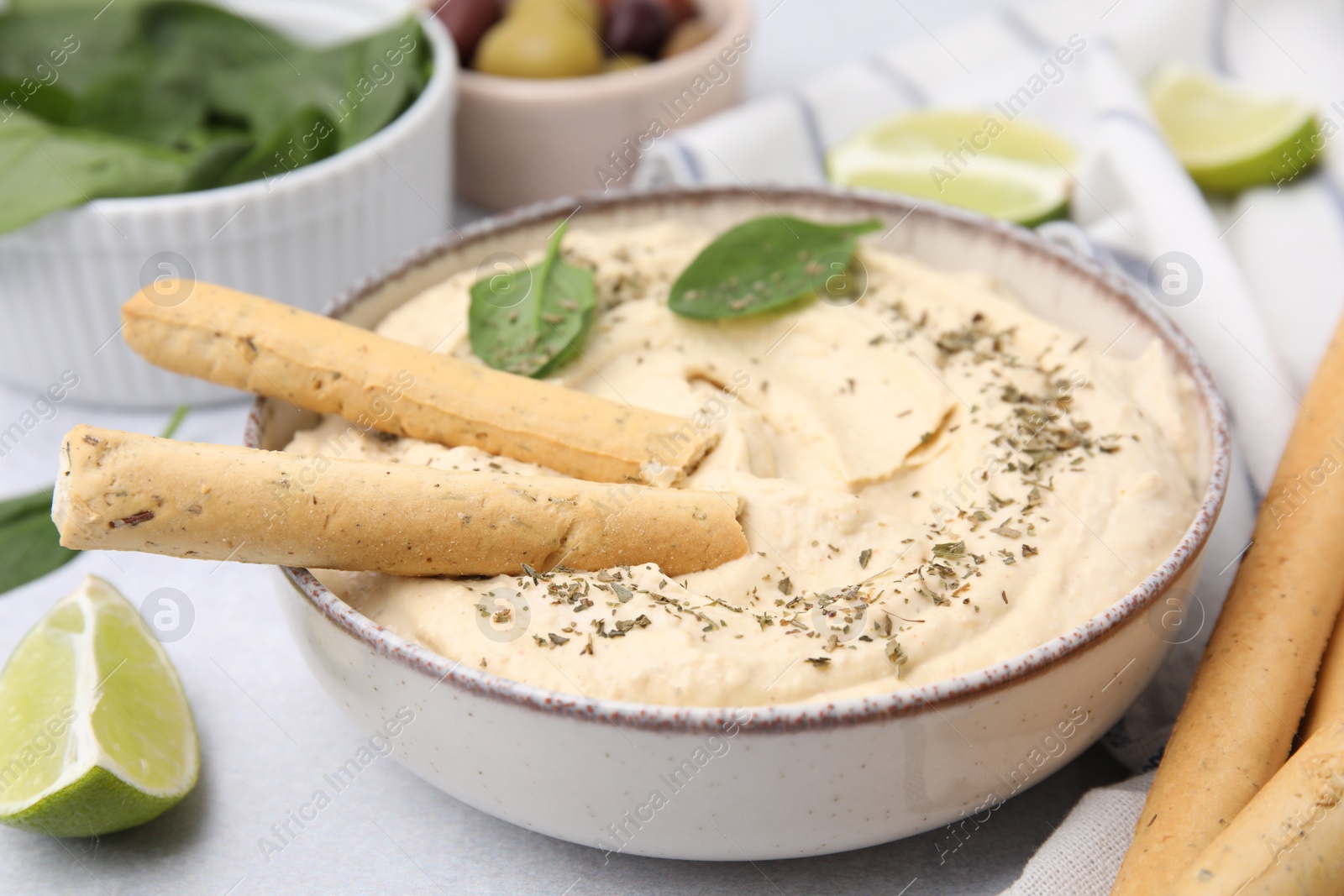Photo of Delicious hummus with grissini sticks on light grey table, closeup