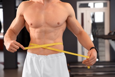 Athletic man measuring waist with tape in gym, closeup