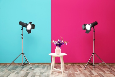 Photo of Professional lighting equipment and vase with flowers on table near wall in photo studio