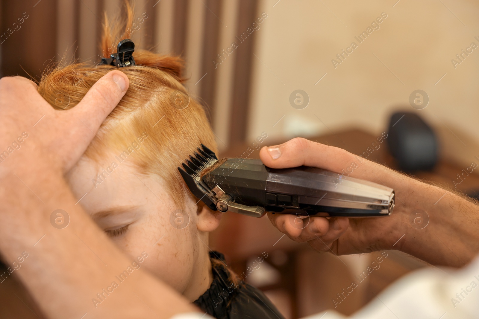 Photo of Professional hairdresser cutting boy's hair in beauty salon, closeup