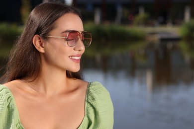 Photo of Beautiful smiling woman in sunglasses near river, space for text