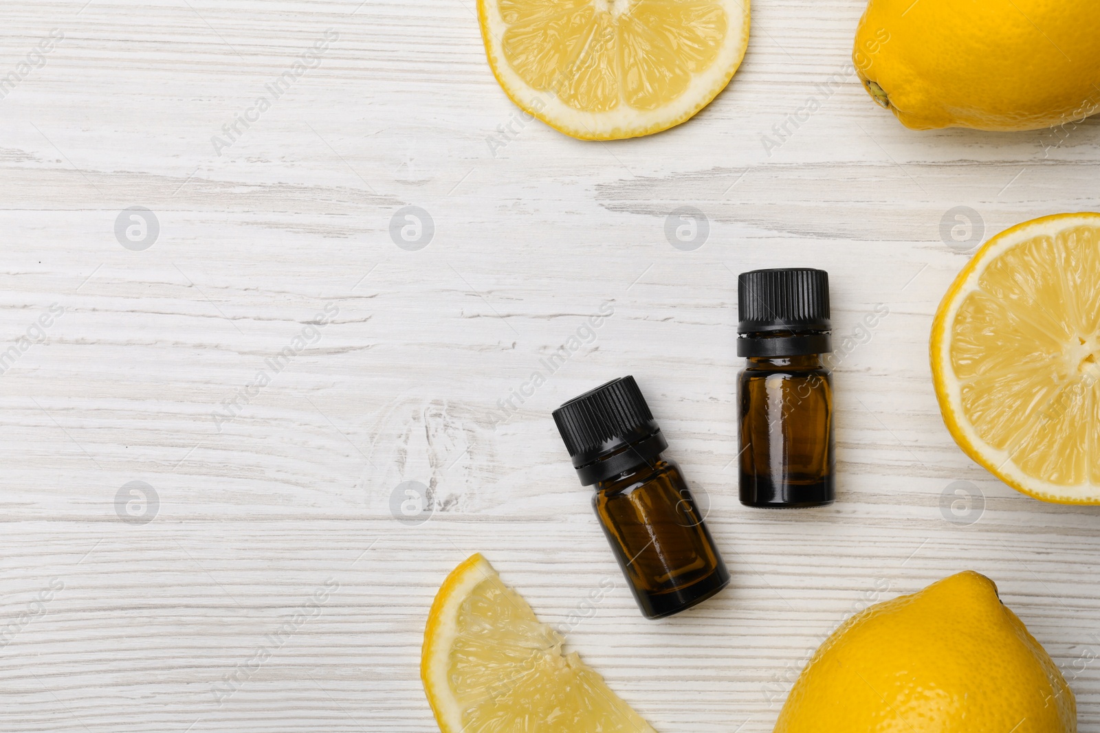 Photo of Bottles of citrus essential oil and fresh lemons on white wooden table, flat lay. Space for text