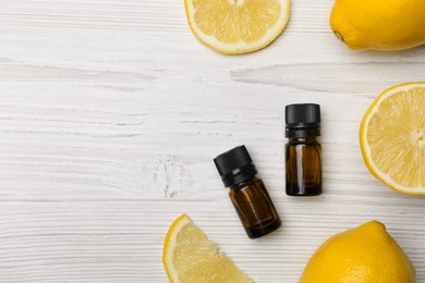 Photo of Bottles of citrus essential oil and fresh lemons on white wooden table, flat lay. Space for text