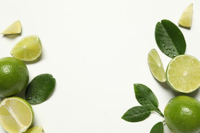 Whole and cut fresh ripe limes with green leaves on white background, flat lay