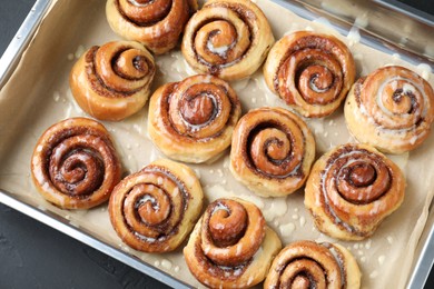 Photo of Baking dish with tasty cinnamon rolls on dark table, top view