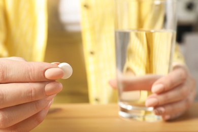 Woman with pill and glass of water at table, closeup