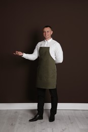 Photo of Full length portrait of happy young waiter in uniform near brown wall indoors