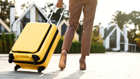 Photo of Woman with yellow suitcase outdoors. Moving day