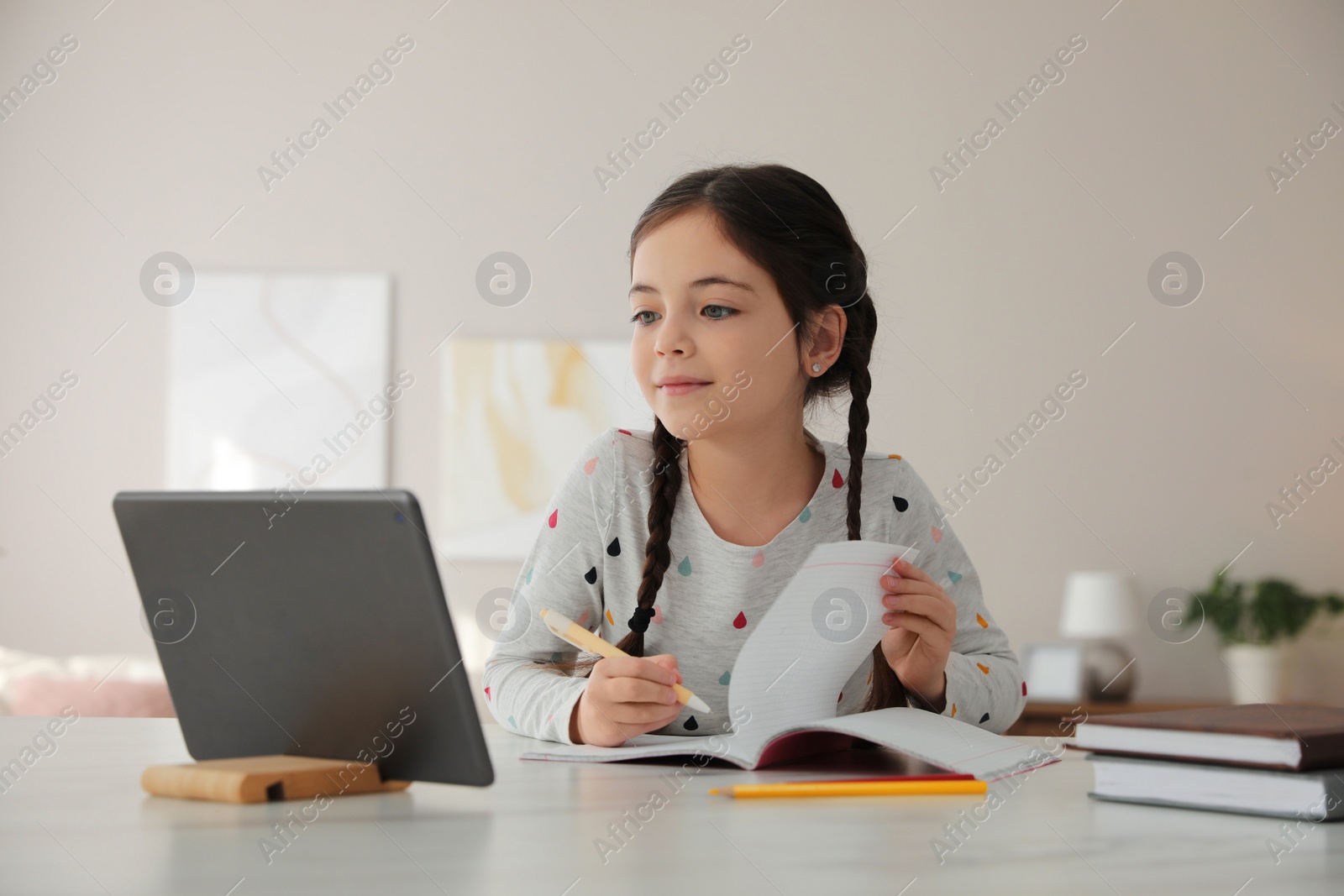 Photo of Little girl doing homework with modern tablet at home