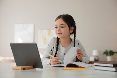 Little girl doing homework with modern tablet at home