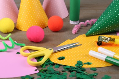 Photo of Different stationery and materials for creation of colorful party hats on wooden table. Handmade decorations
