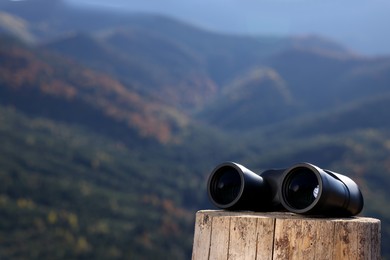 Photo of Modern binoculars on wooden stump outdoors, space for text
