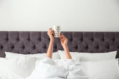 Woman with cup of coffee in bed, closeup. Lazy morning