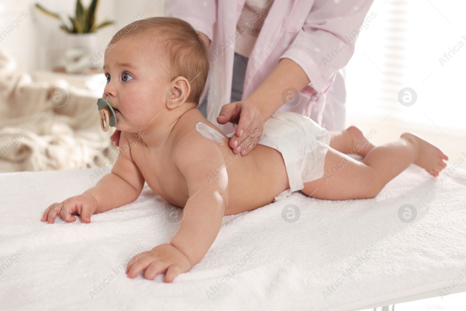 Photo of Mother applying body cream on her little baby at home, closeup