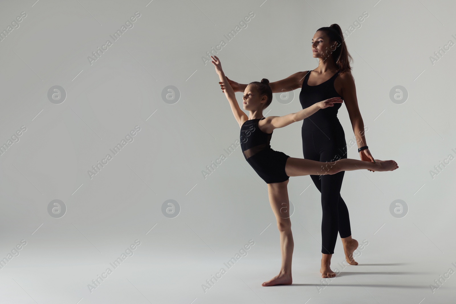 Photo of Gymnastic coach helping little girl to do exercise on white background