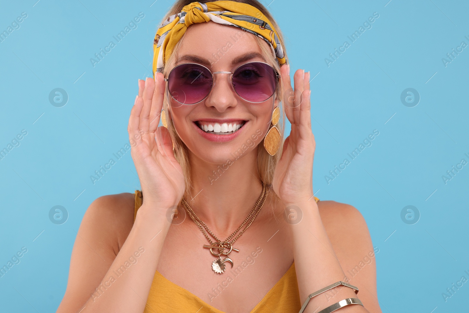 Photo of Portrait of smiling hippie woman in sunglasses on light blue background