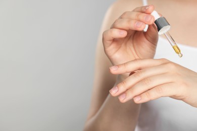 Photo of Woman applying essential oil onto hand on grey background, closeup. Space for text