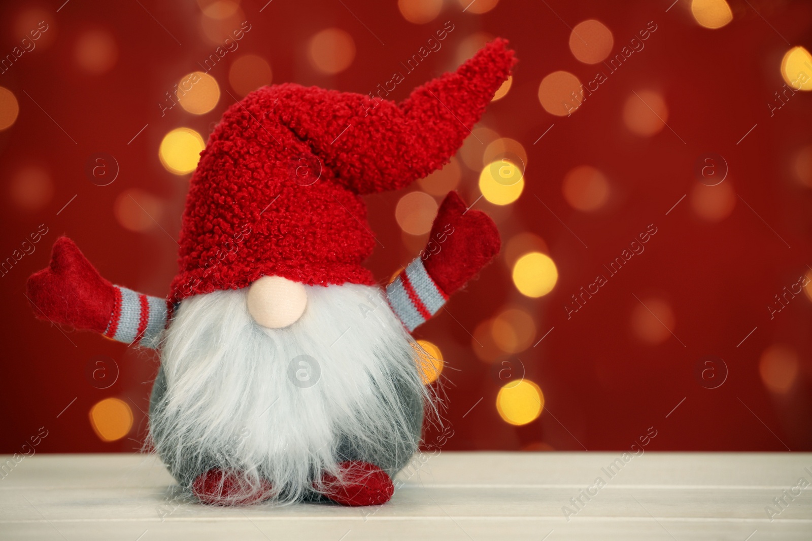 Photo of Cute Christmas gnome on white wooden table against blurred festive lights. Space for text