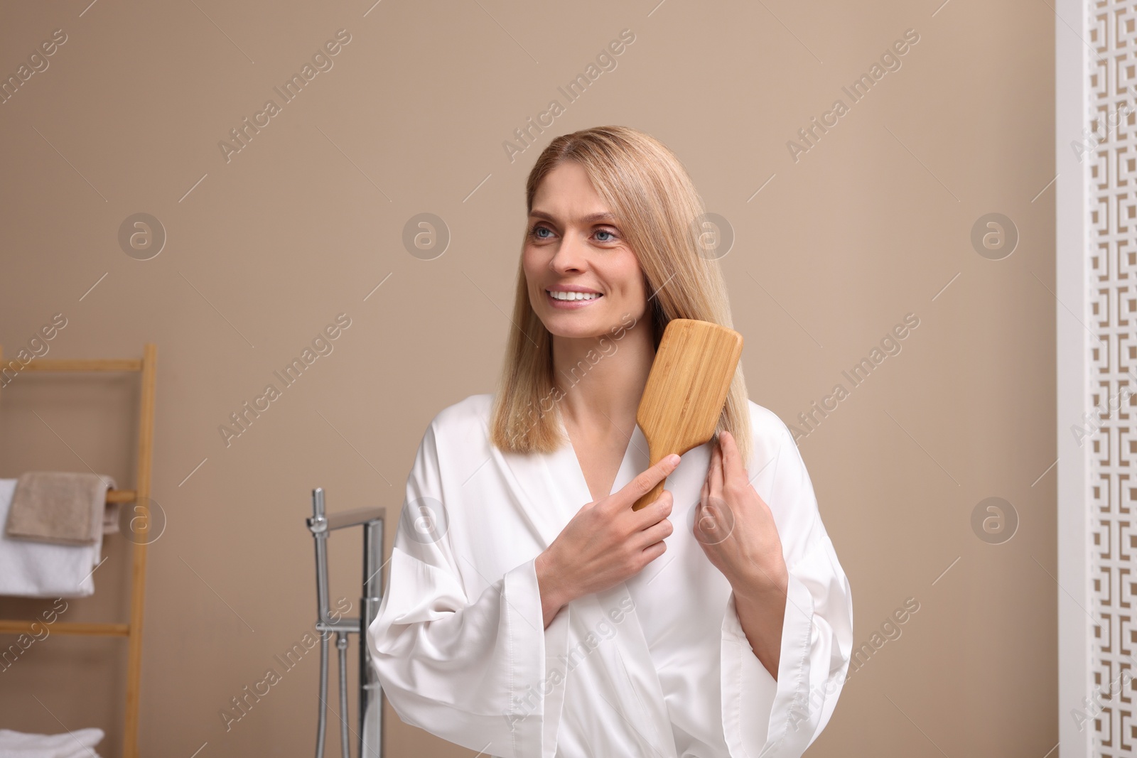 Photo of Beautiful woman in white robe brushing her hair indoors