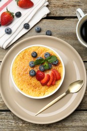Delicious creme brulee with berries and mint in bowl on wooden table, flat lay