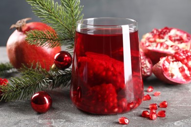 Photo of Aromatic Sangria drink in glass, Christmas decor and pomegranates on grey textured table, closeup