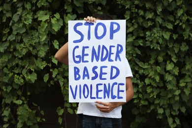 Photo of Woman holding sign with text Stop gender based violence outdoors