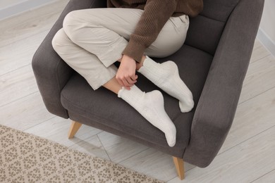 Photo of Woman in warm socks relaxing on armchair at home, closeup