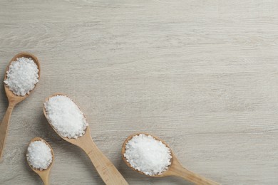 Spoons with natural sea salt on light wooden table, flat lay. Space for text