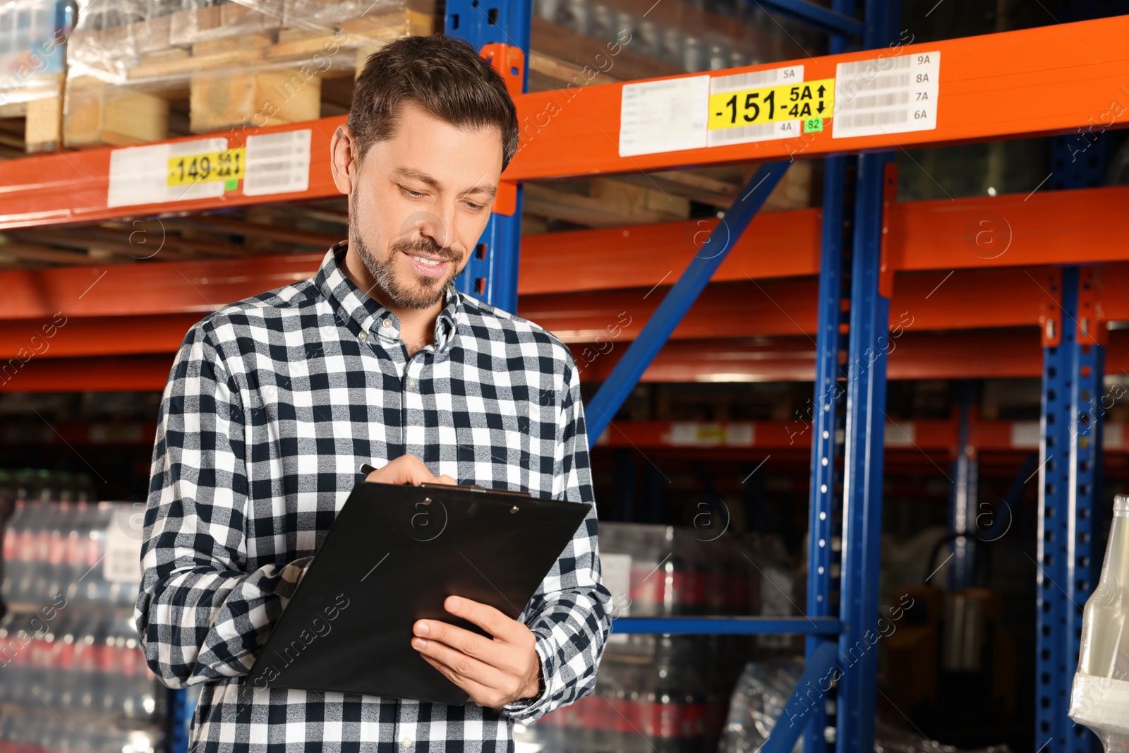 Photo of Happy manager holding clipboard in warehouse with lots of products