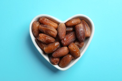 Photo of Heart shaped bowl with sweet dried date fruits on color background, top view