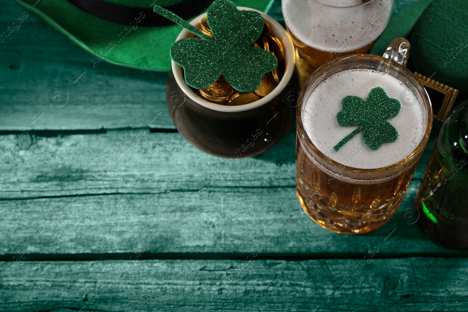 Image of St. Patrick's day. Beer, leprechaun pot of gold and decorative clover leaves on green wooden table, above view. Space for text