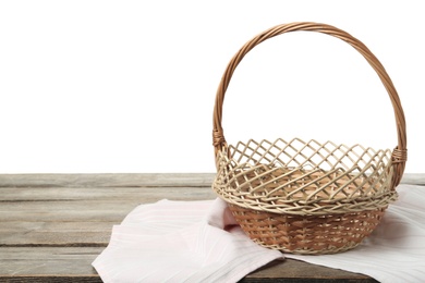 Empty wicker basket and cloth on wooden table against white background, space for text. Easter holiday