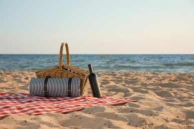 Photo of Blanket with picnic basket and bottle of wine on sandy beach near sea, space for text