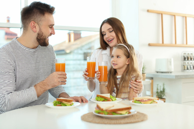 Photo of Happy family having breakfast with sandwiches at table in kitchen